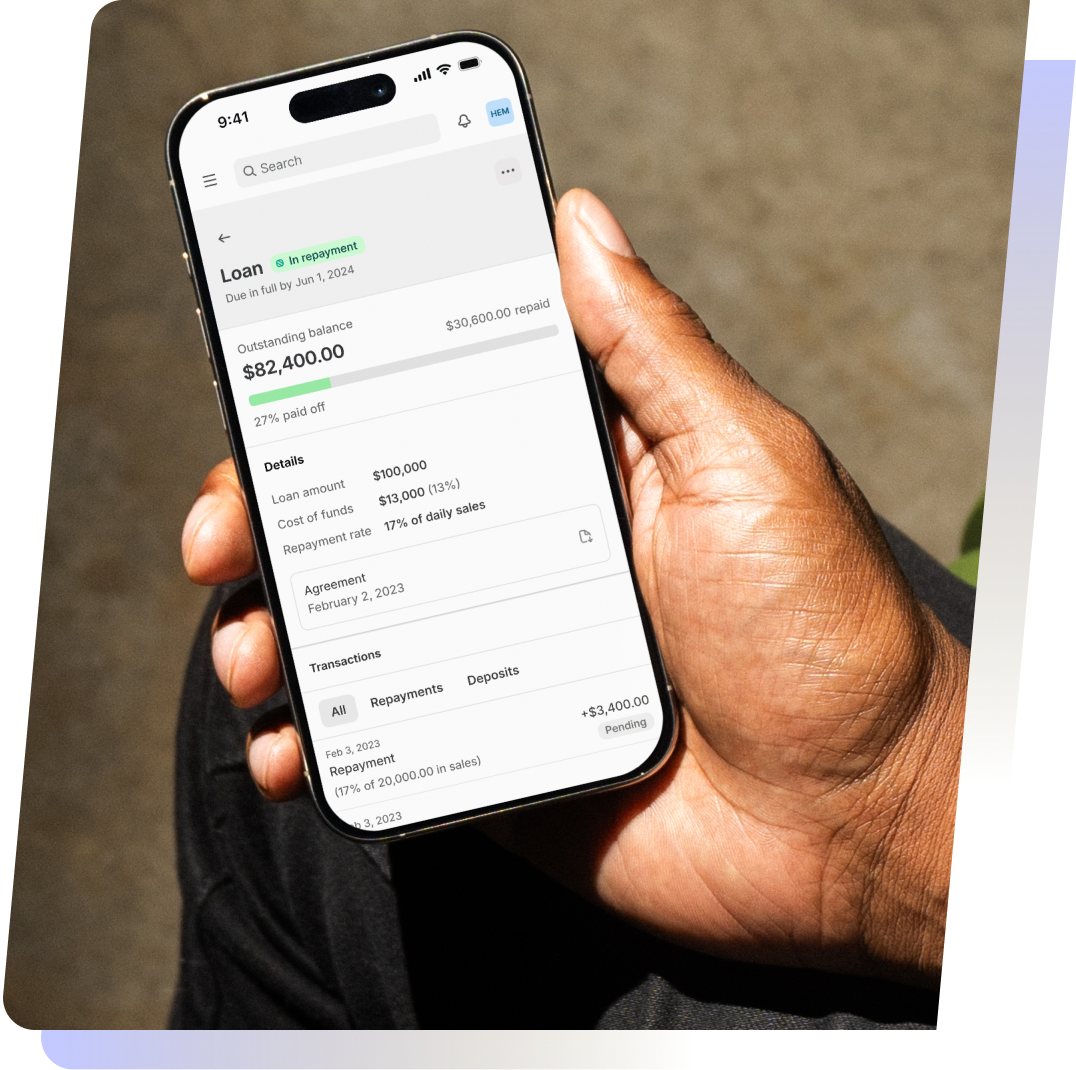 A hand holds a smartphone displaying a funding overview with an outstanding balance of $82,400 and repayment details.