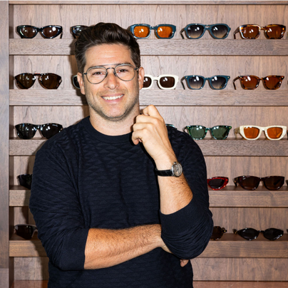 Gary Black, fundador y presidente de Black Optical, sonríe delante de una pared de gafas de sol a la moda.