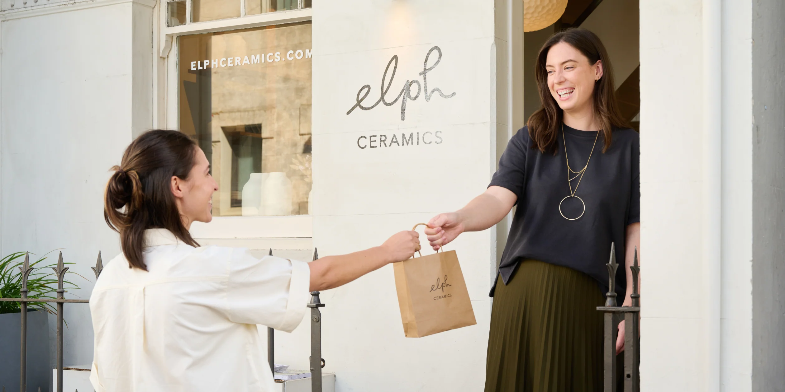 Twee verkoopmedewerkers helpen klanten aan de toonbank met behulp van Shopify POS-hardware. De ene gebruikt het baliesysteem om af te rekenen en de andere verwerkt een afhaling in de winkel op POS Go.