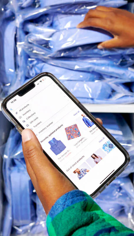 Foto de un empleado de la marca de ropa Kirrin Finch usando las herramientas de inventario de Shopify en el dispositivo móvil para preparar un pedido de camisas