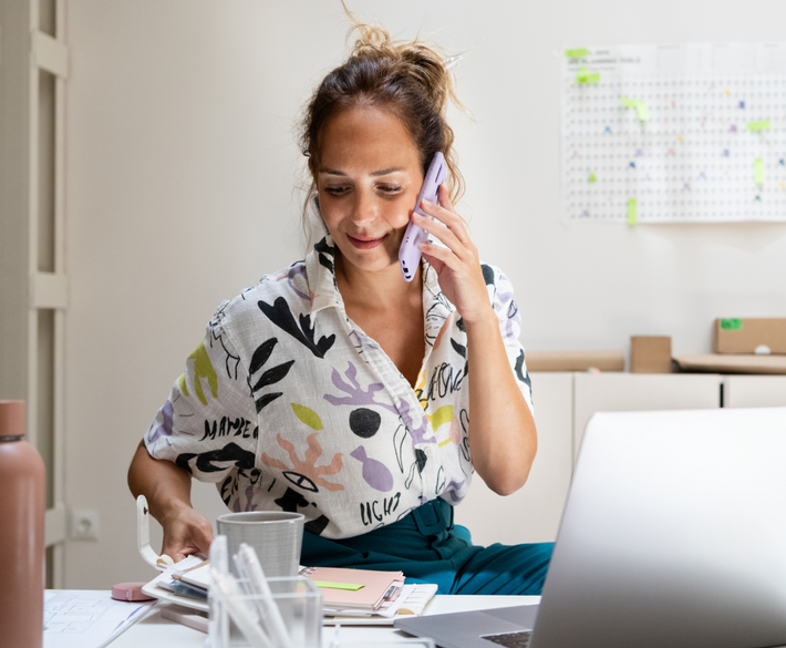 A white female Shopify merchant on the phone, reviewing her planner, in her office