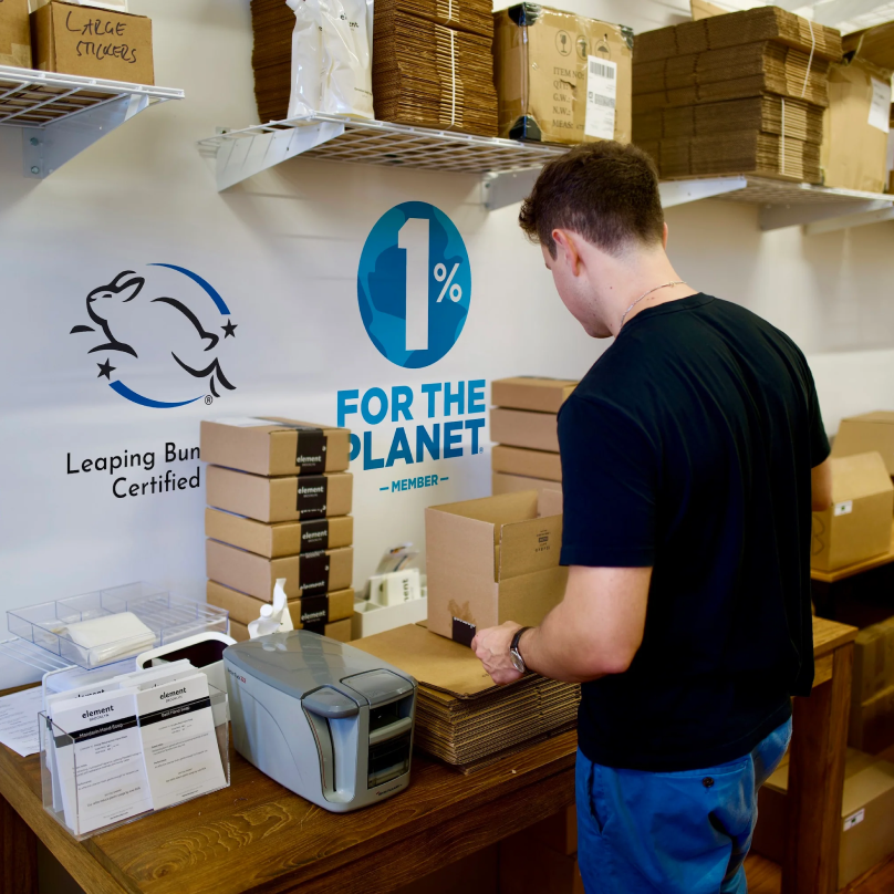Un hombre en una estación de envíos armando cajas de cartón junto a una impresora de etiquetas de envío