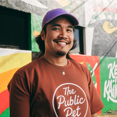 Jordan Lee, propietario de The Public Pet, sonríe orgulloso delante de un mural al aire libre y viste una camiseta de The Public Pet.