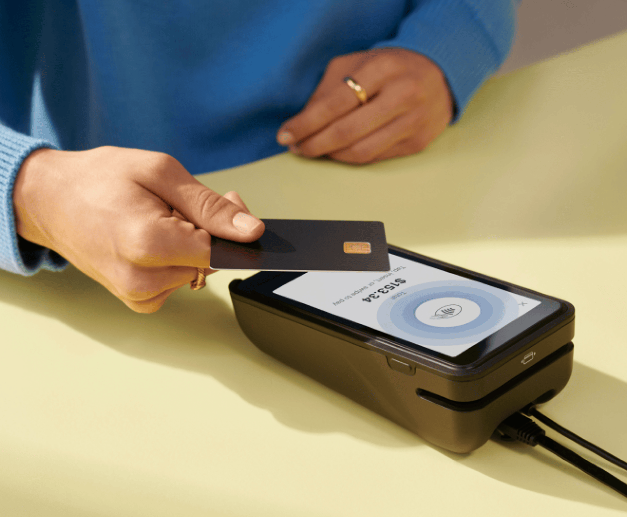 A customer taps their payment card on Shopify POS Terminal’s screen.