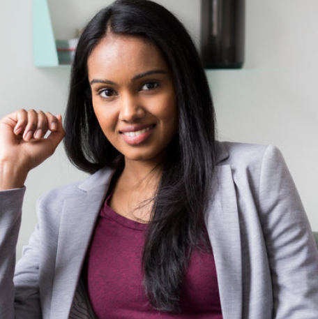 The image features asmiling woman sitting in a chair，wearing a gray suit and a red blouse.She is posing for a photo，and her hands are raised in a confident pose.The woman appears to be a professional，and her attire suggests a foral setting。