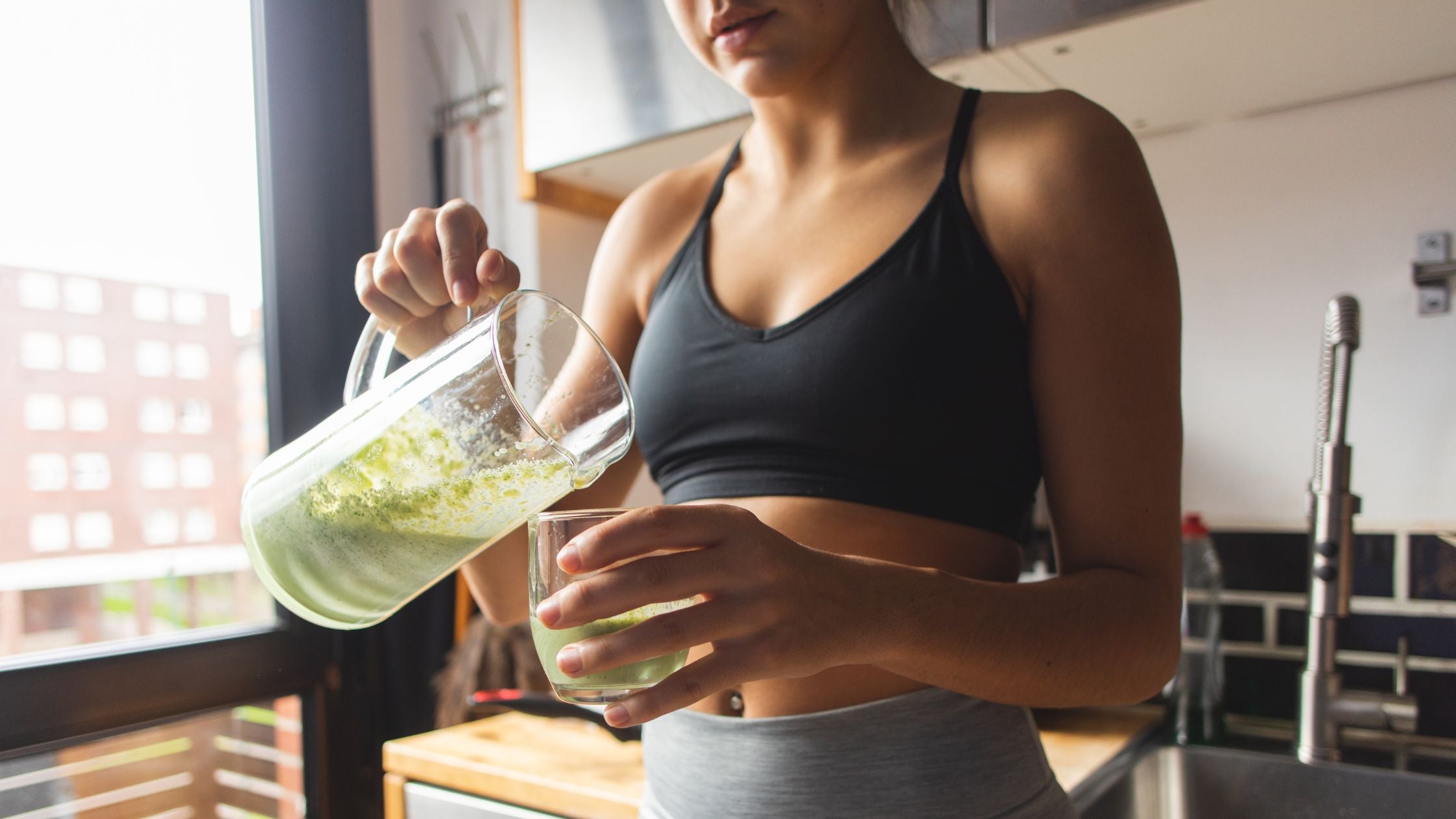 A young woman fills up her glass with a superfood smoothie made with PINES Wheat Grass powder.
