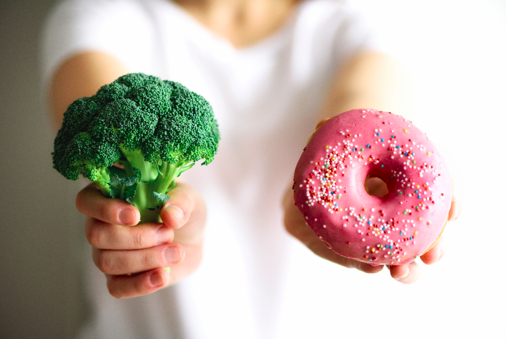 how to stop eating junk food: Woman holding a broccoli and donut