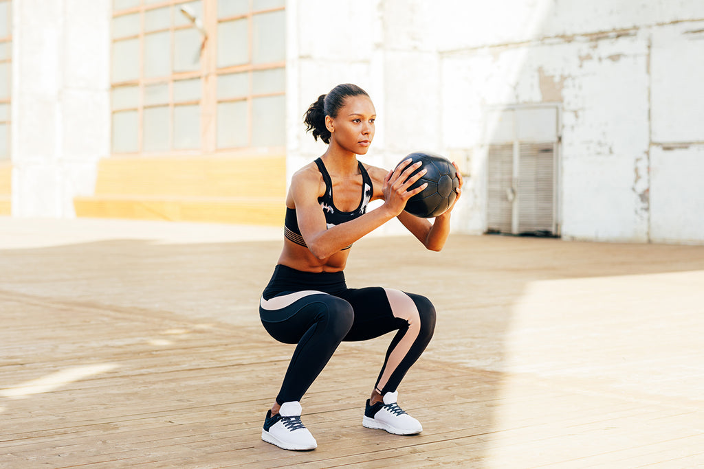 Female doing sissy squats exercise with medicine ball
