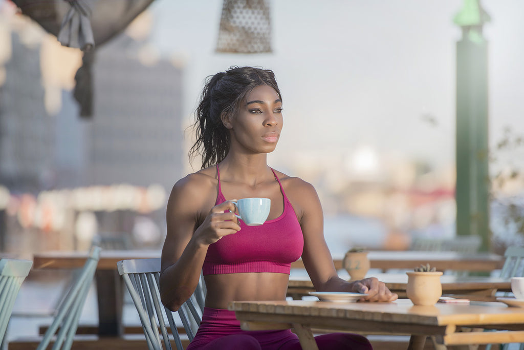 coffee before workout: woman in a sports outfit and holding a cup of coffee