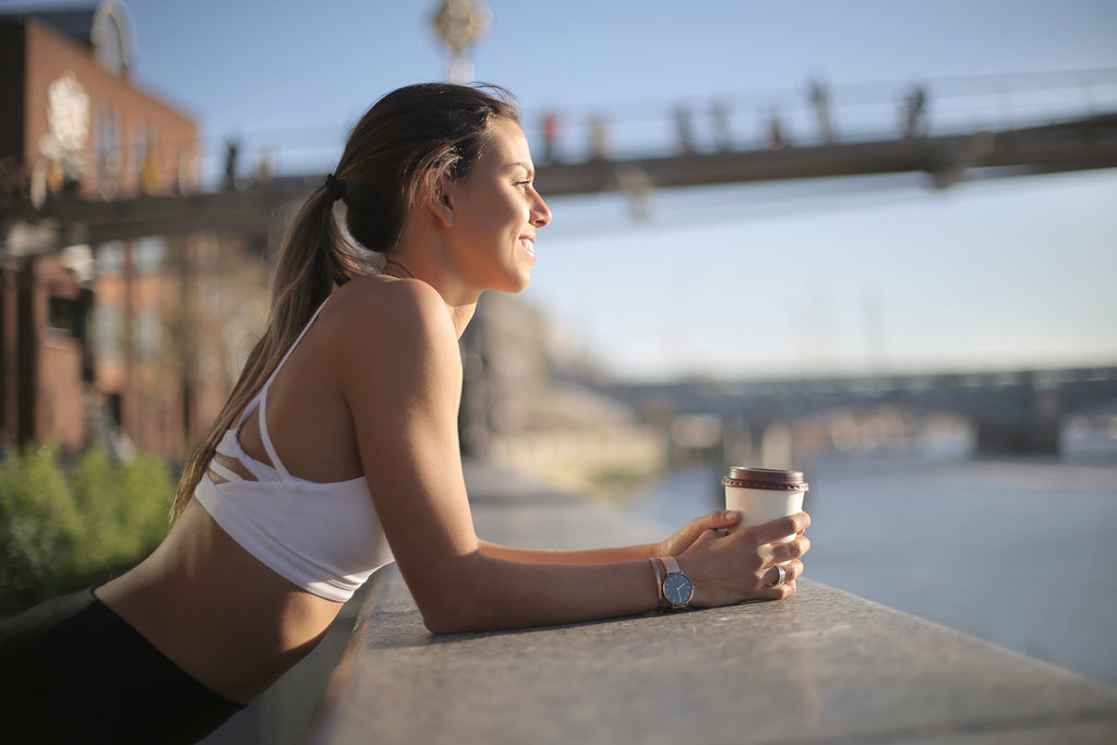 coffee before workout: woman in a sports outfit having coffee while looking at the river