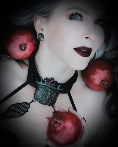Kari wearing a serpent top, in a crocodile fossil and garnet talisman, surrounded by pomegranates.