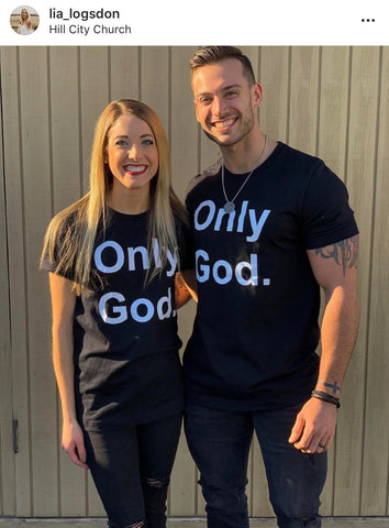 White couple wearing black Only God unisex tshirt.