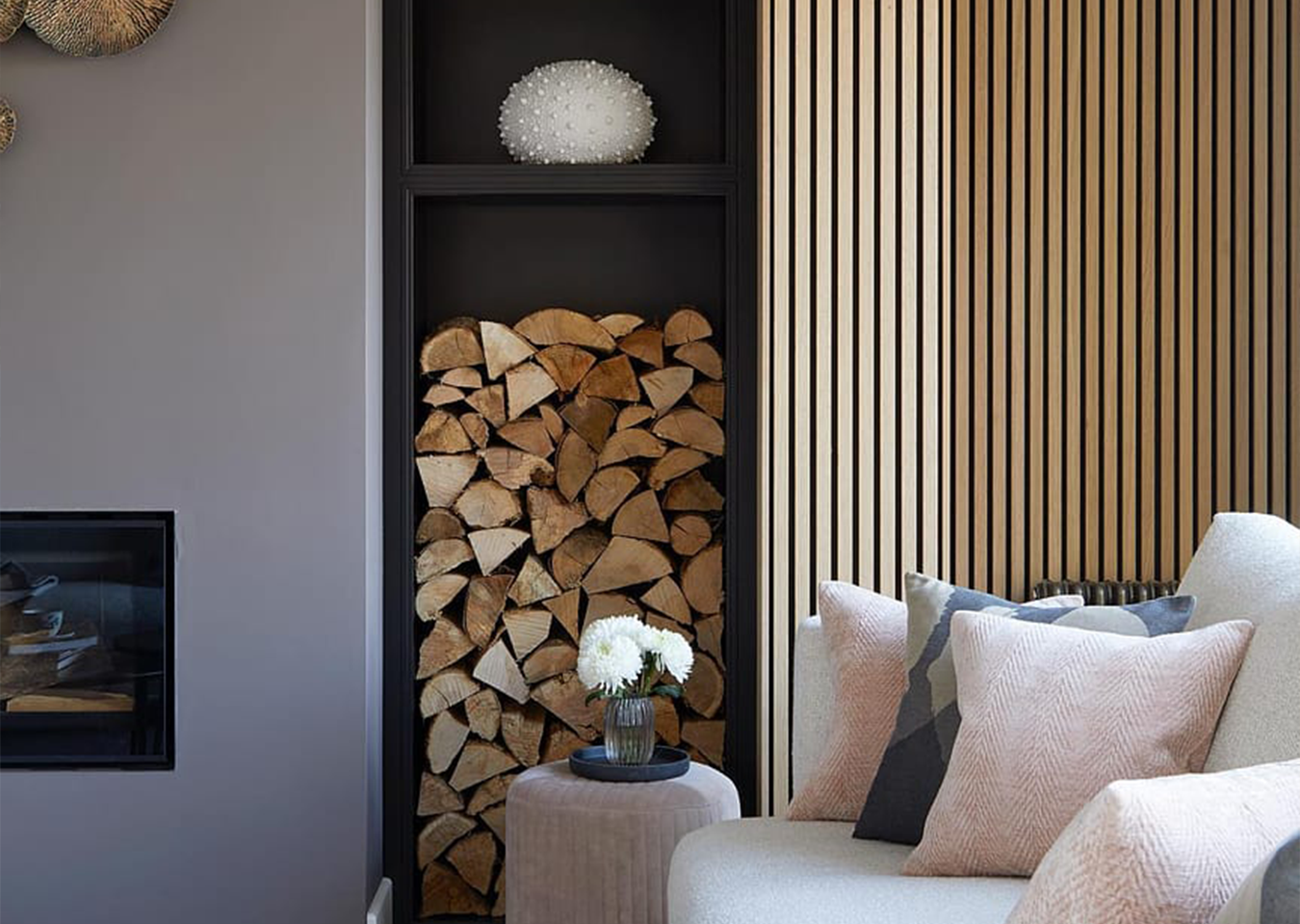 Log in storage in living room. End of sofa in foreground. Slatwall on wall to the right.