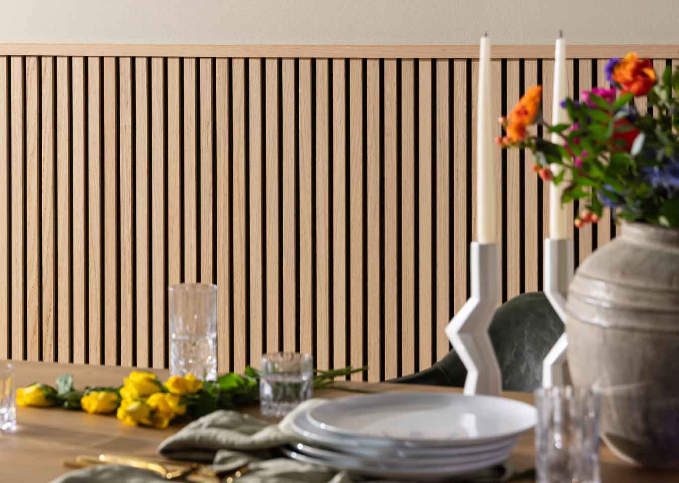 SlatWall Midi Natural Oak panels and Top Trim on a dining room wall behind a table laid with flowers, candles, plates and glasses.