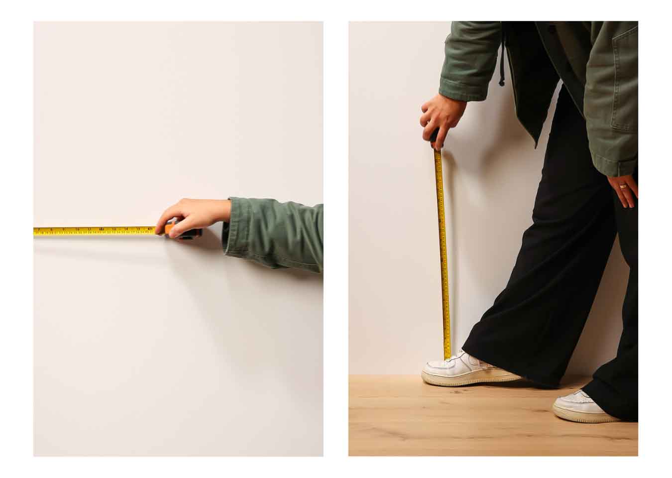 A person wearing a green jacket, black trousers and white trainers measuring a wall with a yellow measuring tape.