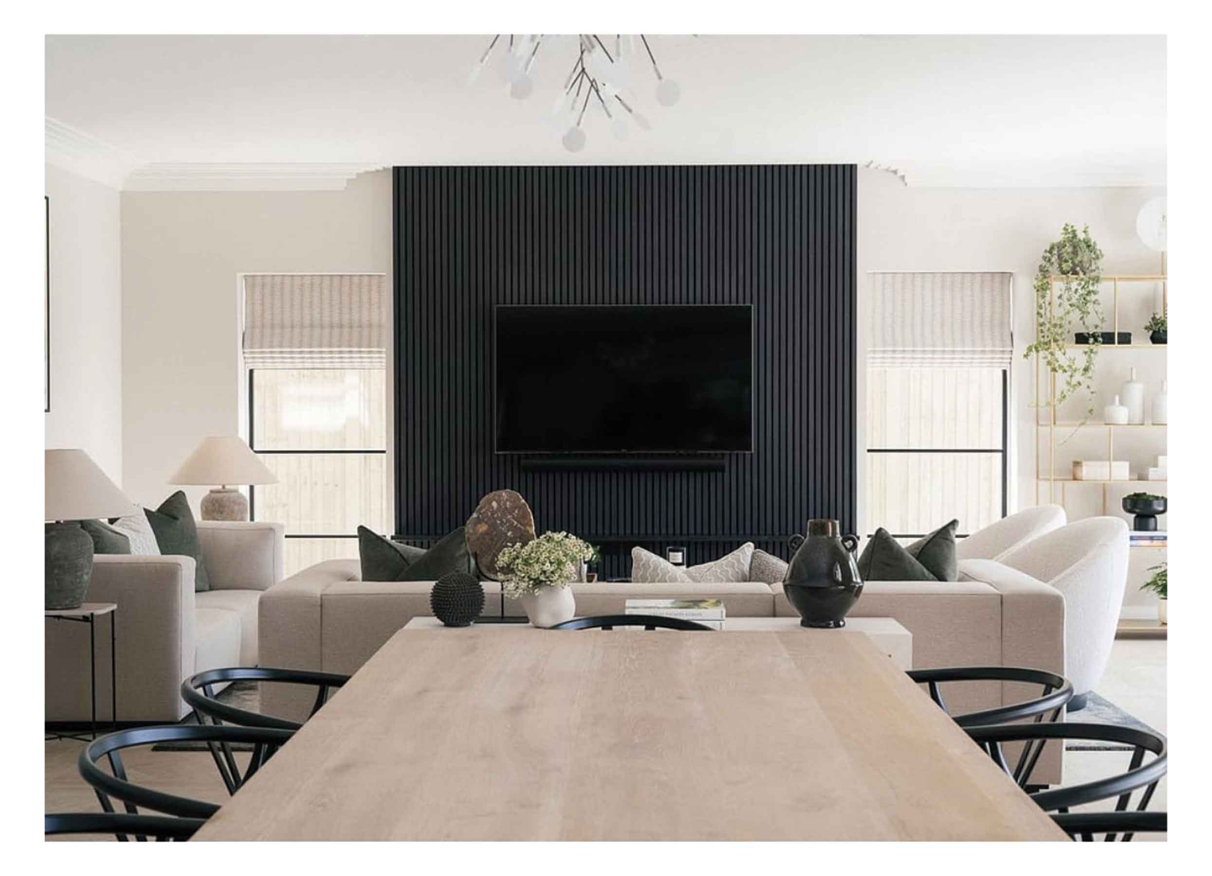 Open-plan living room with neutral walls and sofas, black panels for a media wall, and wood dining table with black chairs.