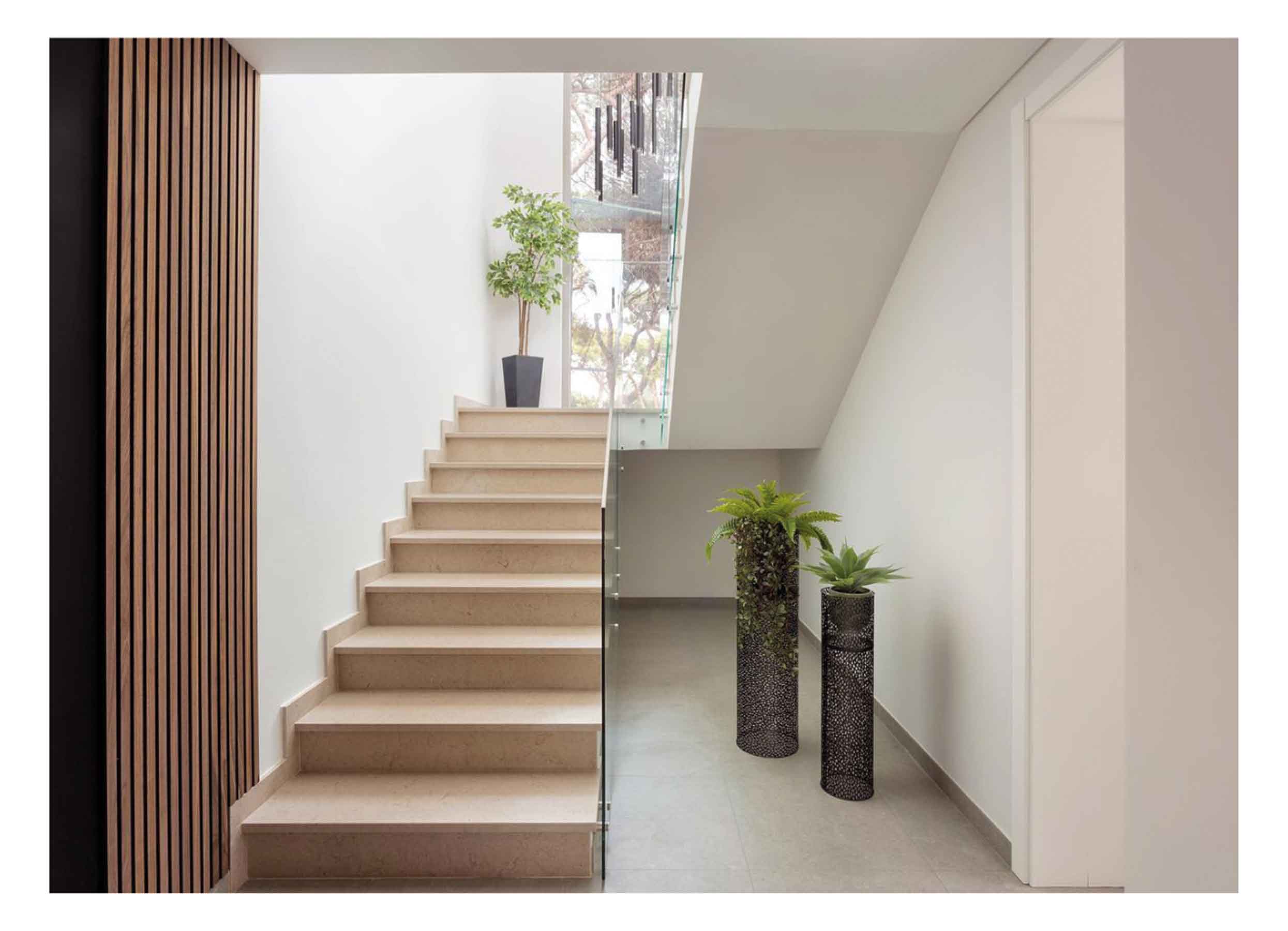 Minimalist staircase with SlatWall Walnut panels, white walls, beige steps, glass banister and houseplants in black vases.