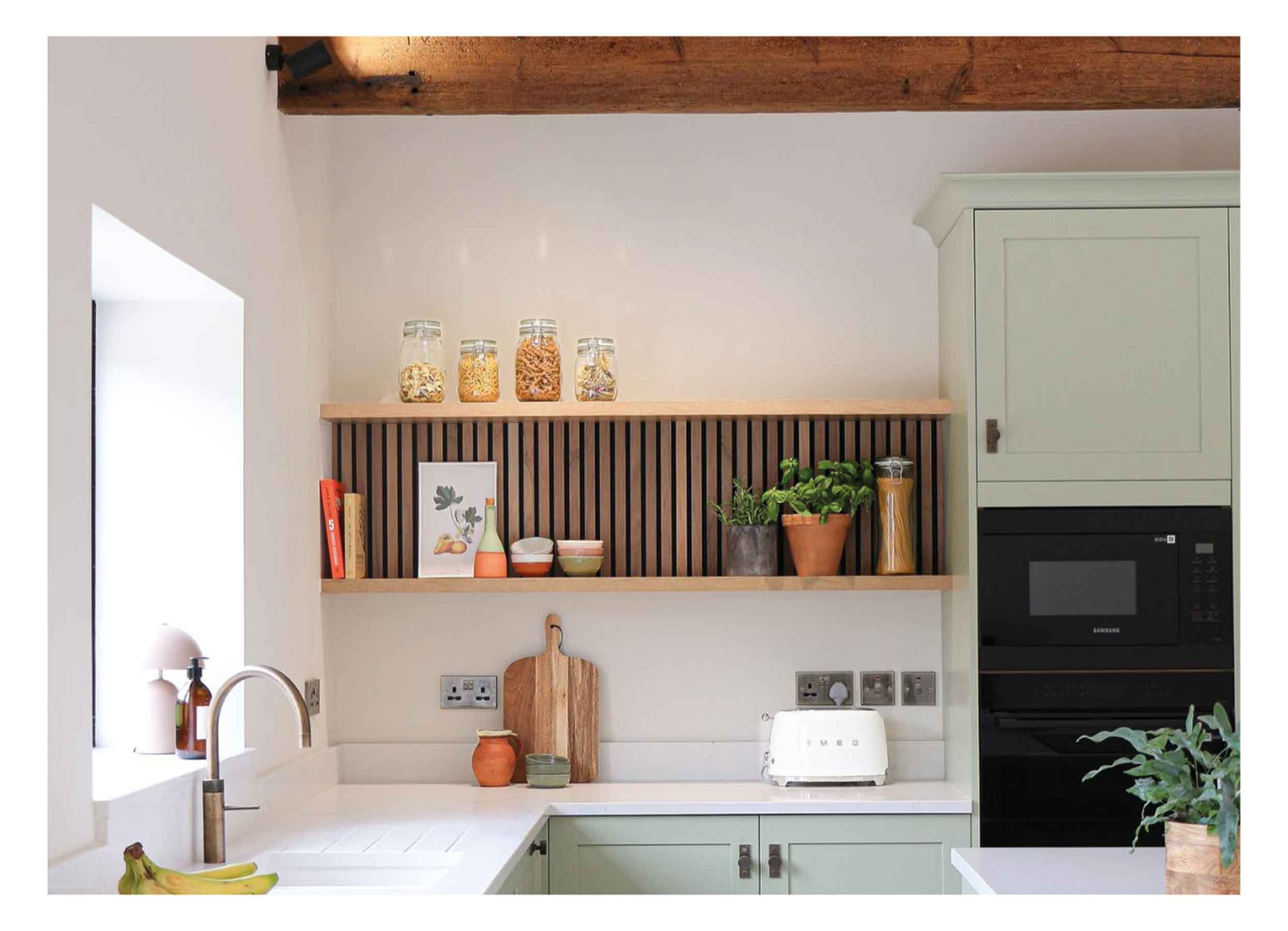 A white farmhouse kitchen featuring wood panels in an alcove shelf above a marble countertop with bowls, jars and plants.