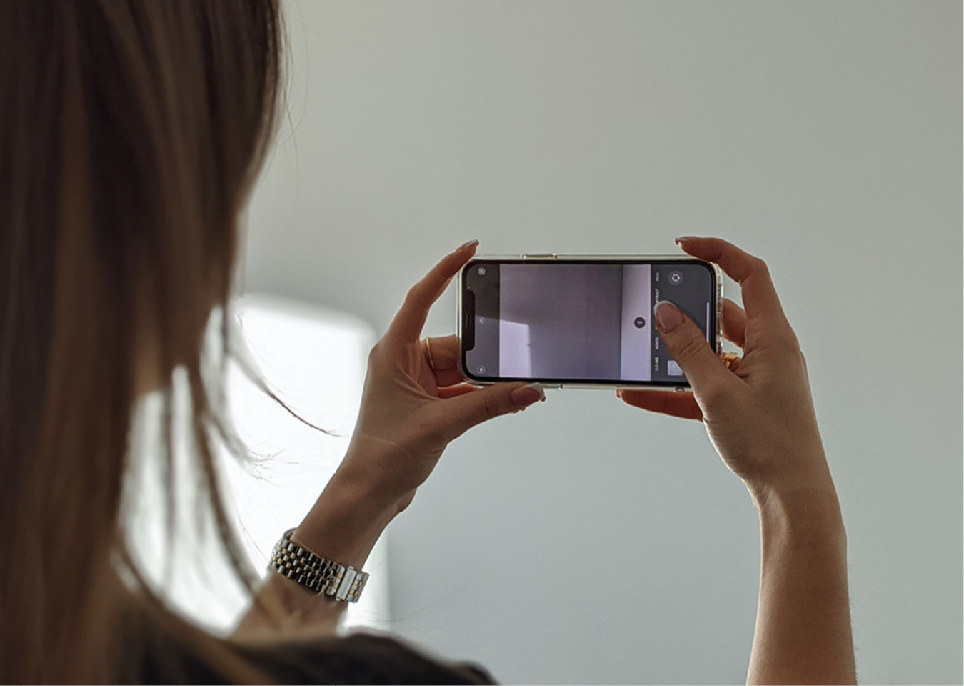 A woman takes a photo on a mobile phone of a blank wall for Naturewall's visualiser tool.