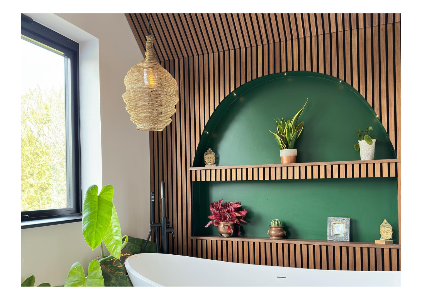 Brown wood panelling with green alcove shelves in a bathroom with a white free-standing bath and houseplants.