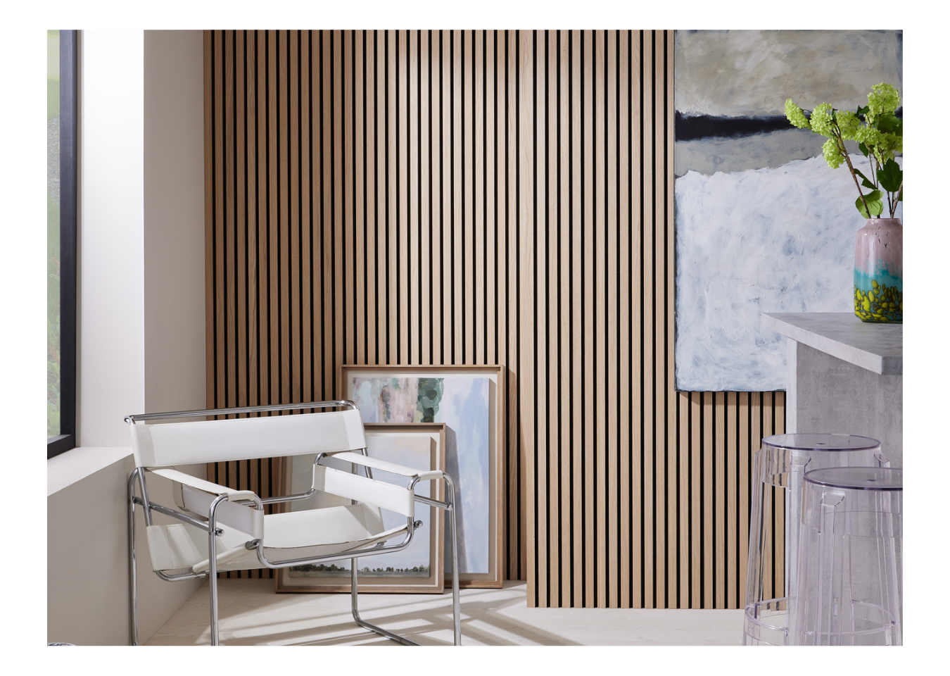 SlatWall Natural Oak panels behind landscape paintings and a white and silver chair next to a window in a biophilic interior.