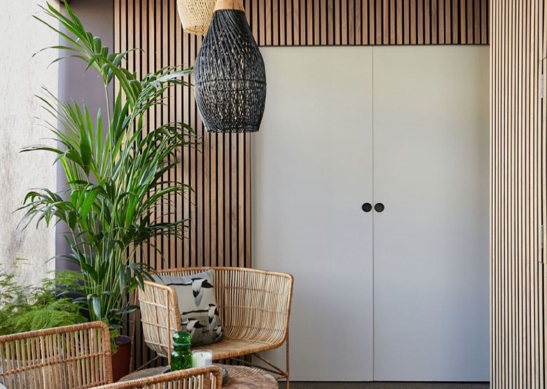 White double doors surrounded by Naturewall Natural Oak on black felt SlatWall panels. Rustic wicker chairs and greenery in foreground.