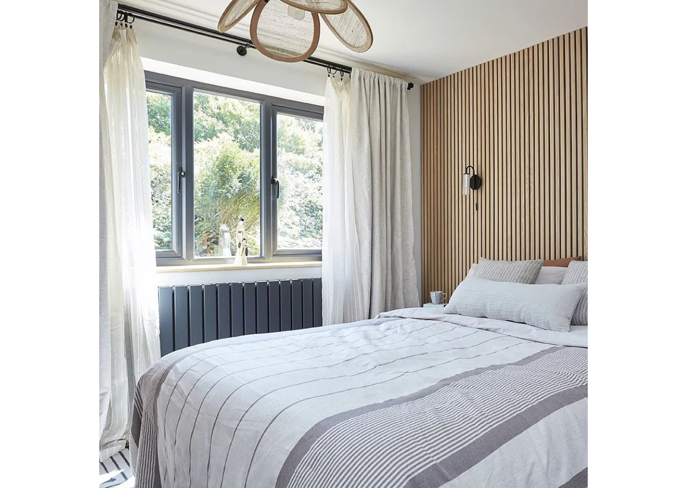 Bed with grey and white bedding. Sheer linen curtains and slatwall scandinavian feature wall behind the bed.