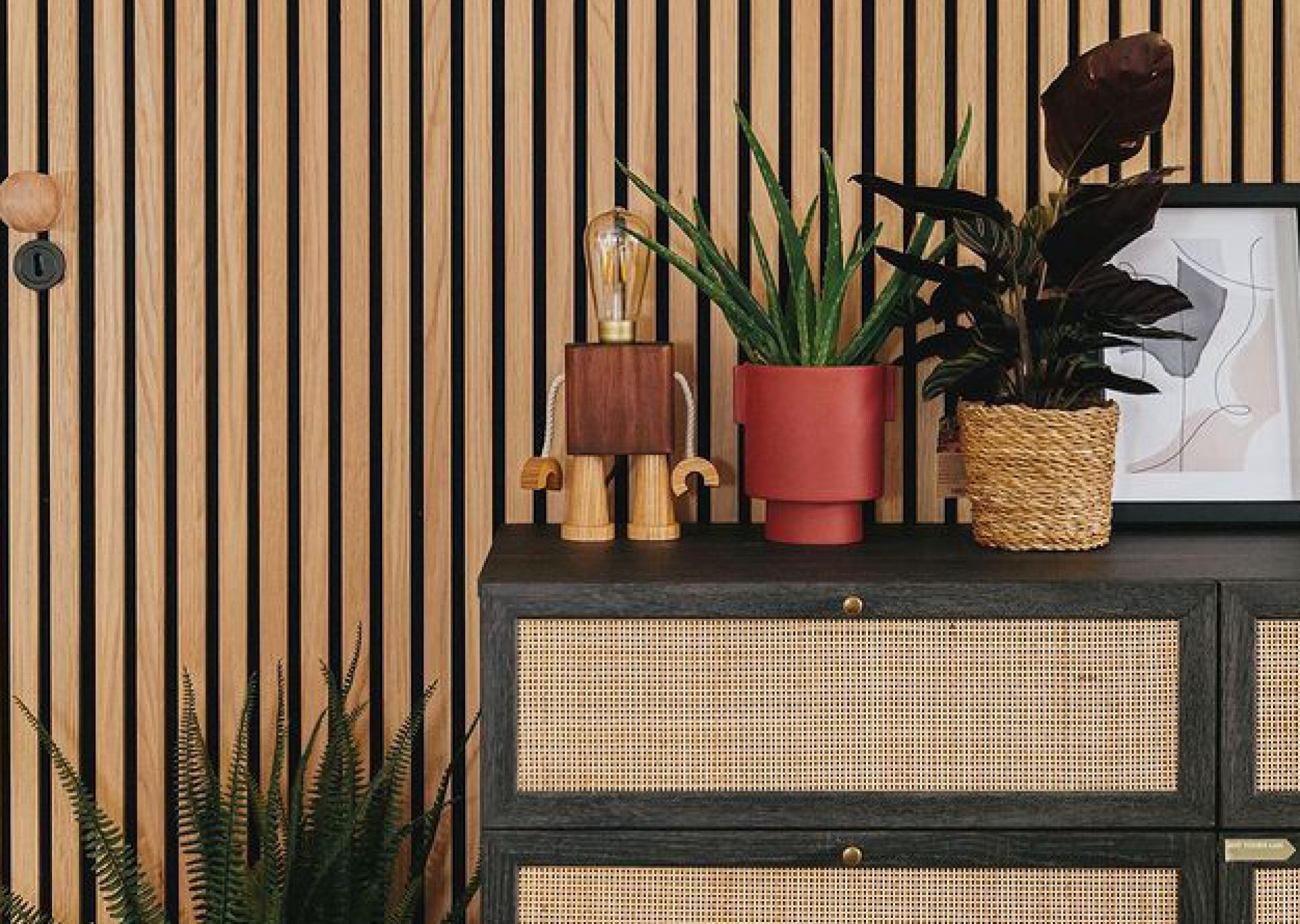 Boho design chest of drawers with plants and wooden lamp on top. Naturewall slatwall panels on the wall behind