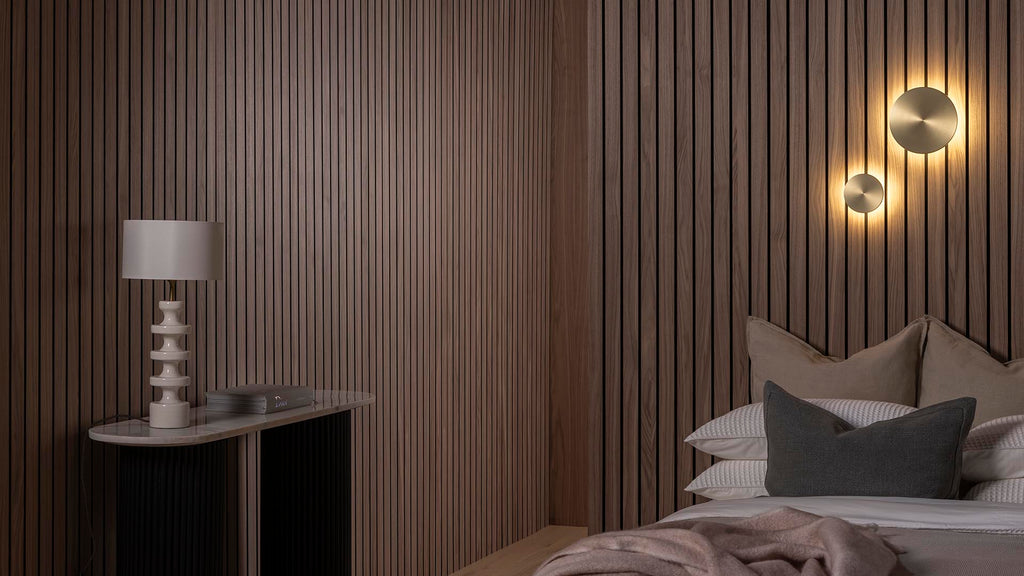 Contemporary bedroom with SlatWall Grand Walnut panels, gold wall lights, a white lamp and a monochrome bed and side table.