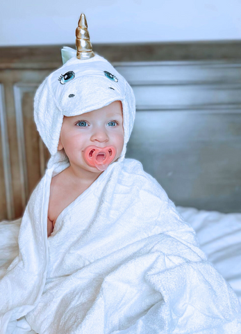 a baby using a pacifier while also wrapped in kloud bambu white unicorn hooded towel