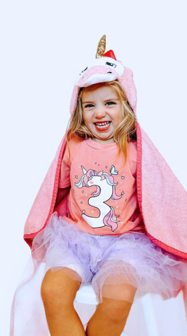 a girl child happily wearing her kloud bambu pink unicorn bamboo hooded towel for the holiday season