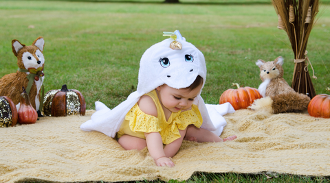 baby playing on the mat outside wearing kloud bambu white unicorn hooded towel during fall season