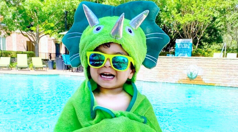 a boy by the pool wearing his kloud bambu green dinosaur bamboo hooded bath towel