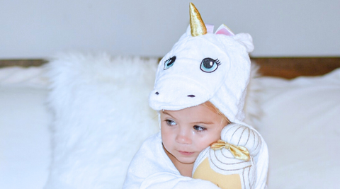 a child holding a doll while wrapped in kloud bambu white unicorn hooded towel
