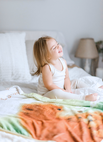 happy baby girl sitting on the bed with her kloud bambu minky blanket