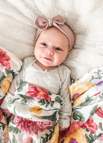 baby lying down wrapped in bamboo floral muslin swaddle blanket