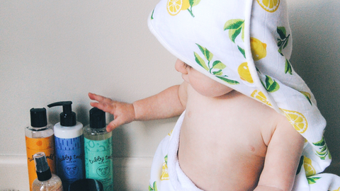 A baby looking at the skin care products while wearing a lemon hooded towel 