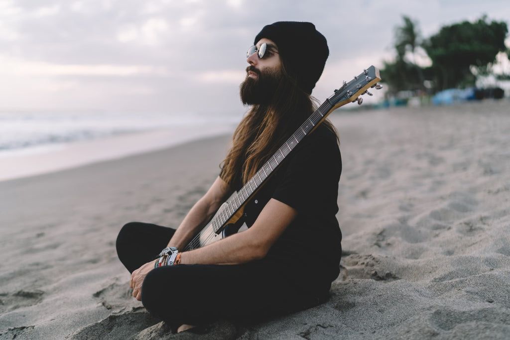 Long Haired Minimalistic Hippy On The Beach At Sunset With A Guitar In Hand