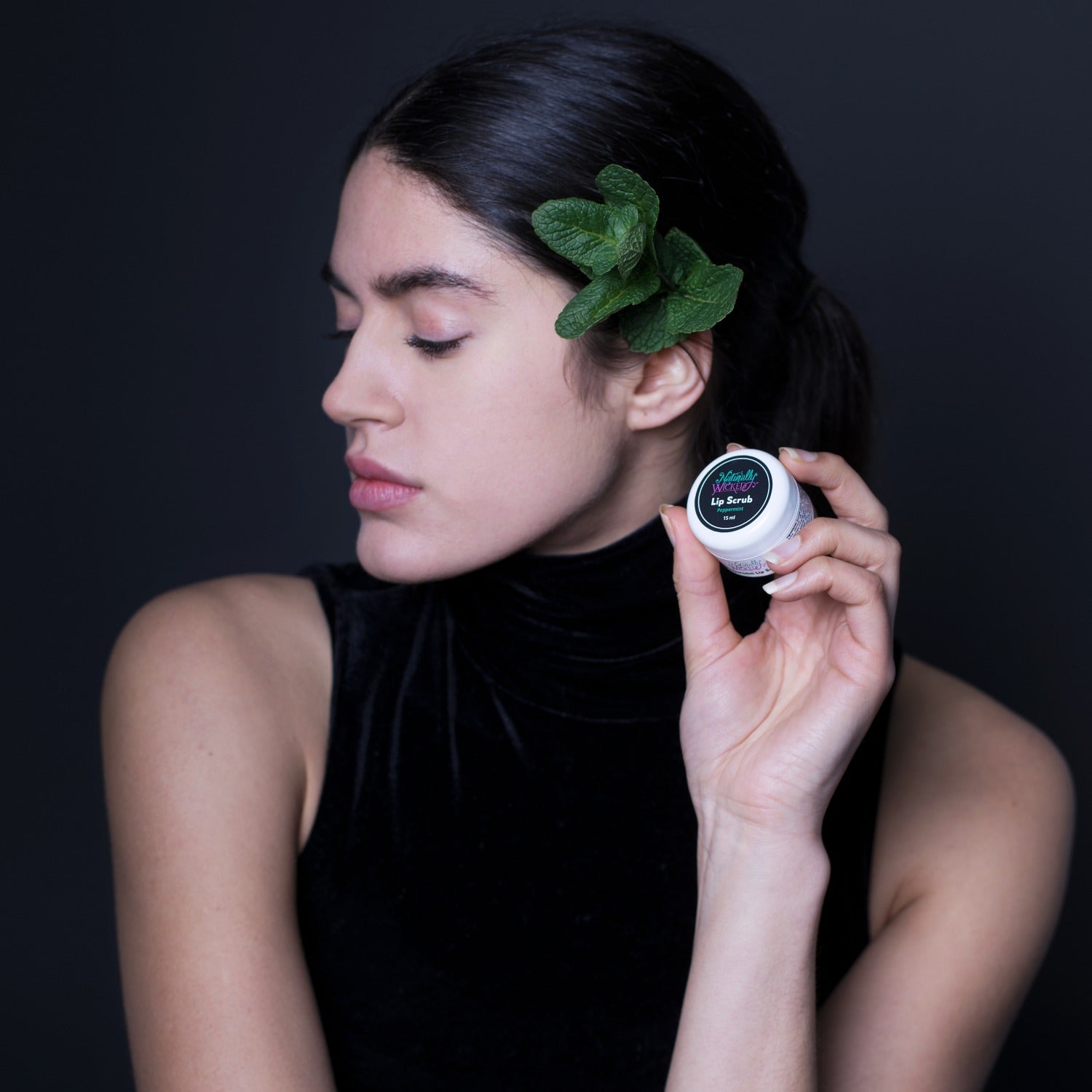 Naturally Wicked Peppermint Lip Scrub In Hands Of Beautiful Dark Haired Lady Decorated With Fresh Green Peppermint Leaves