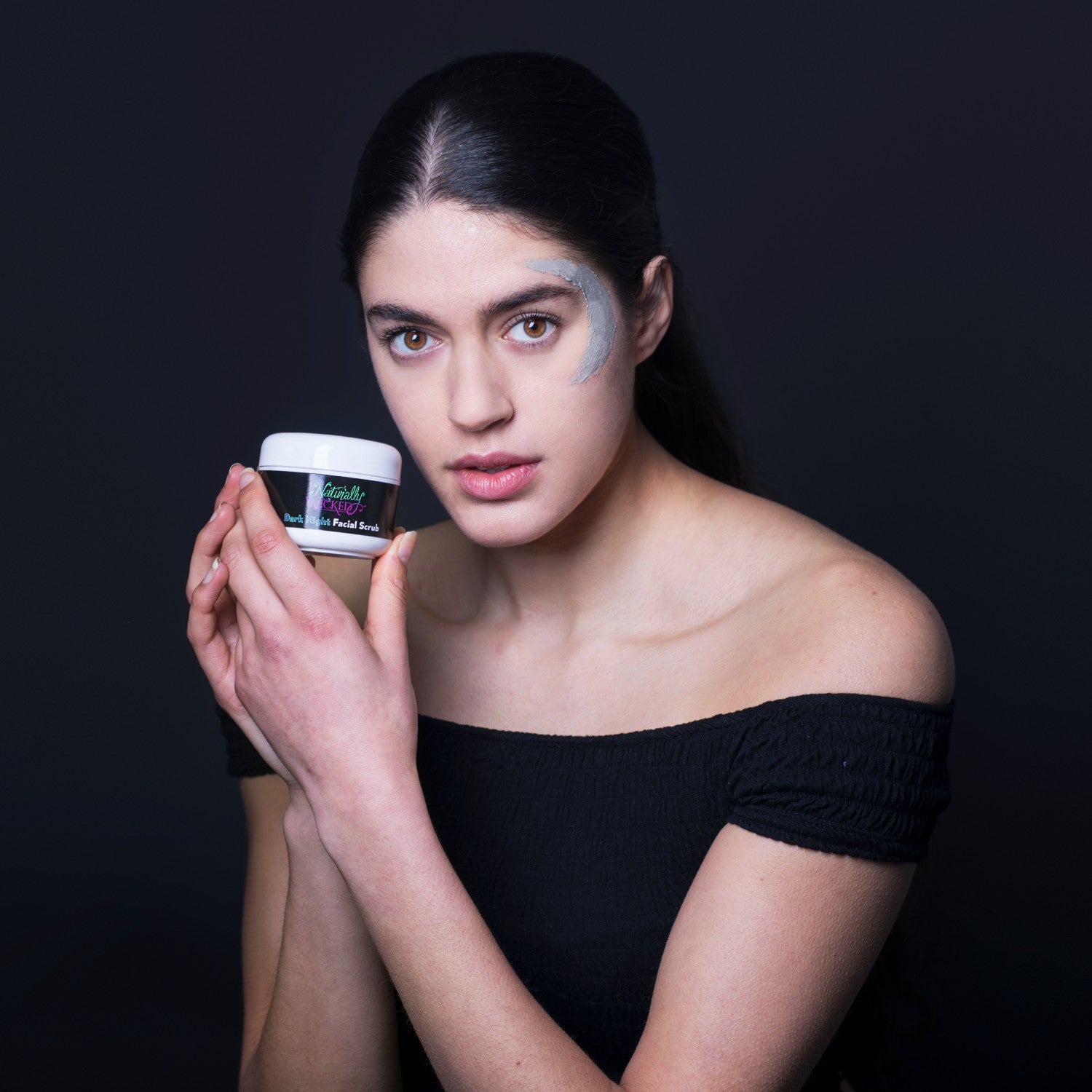 Naturally Wicked Dark Night Facial Scrub In Hands Of Beautiful Dark Haired Woman With Scrub On Face
