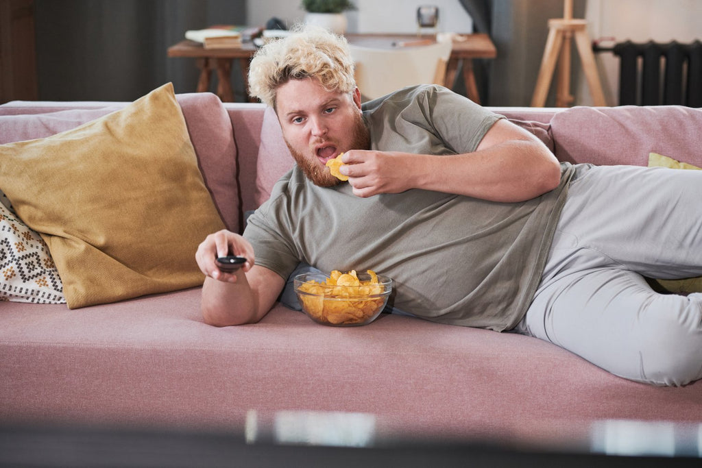 Lazy Man Lay Eating Potato Chips On Chair With Remote In Hand Whilst Watching TV