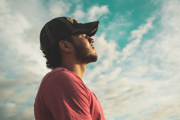 A Man With Cap At Peace With Himself With Eyes Closed And Sky In Background