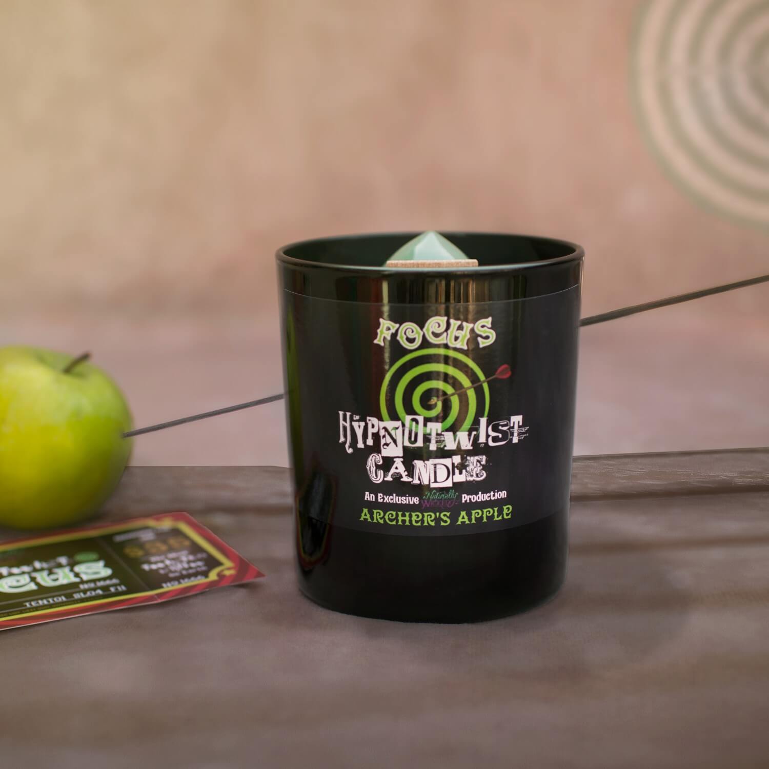 Naturally Wicked Hypnotwist Focus Candle Entombed With Hypnotic Spinning Top Beside Archer's Arrow & Apple