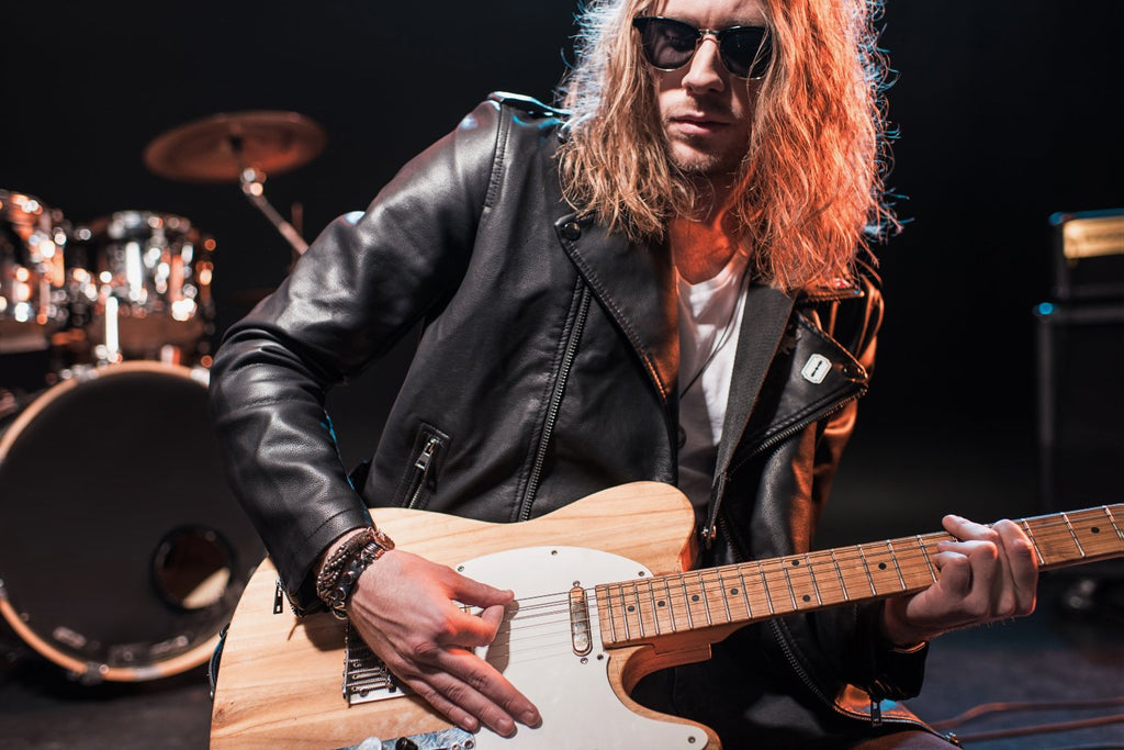 Long Haired Rock Star Looking Cool With Sunglasses On & Guitar In Hand