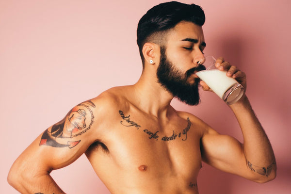 Dark haired man drinking milk topless