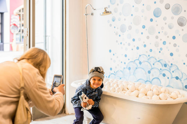 A boy has his picture taken in front of a bathtub with bubbles painted on the wall behind it inside The Scented Market's new store in the Blue Mountain Village.
