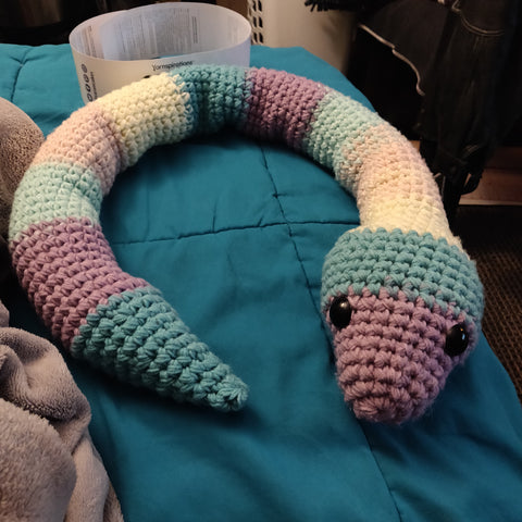 Crochet snake on couch. Snake is a gradient of purple, blue and white.