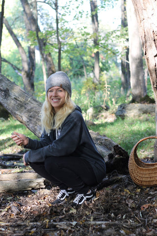 A woman crouched down in the woods holding a foraged mushroom.