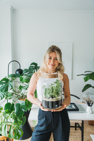 A woman is holding a large, sealed terrarium.