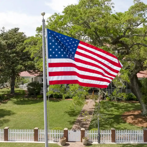 A large American flag waves on a tall flagpole in a well-maintained yard, emphasizing locally sourced flag options.